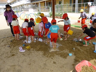 砂場で水遊びをする園児